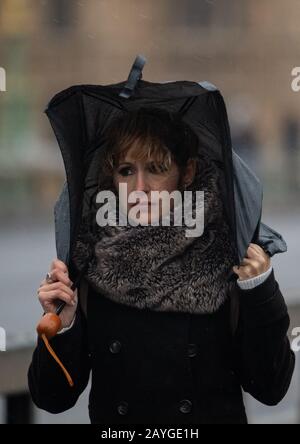 Eine Frau wird von starkem Wind gepufft, wenn sie die Westminster Bridge im Zentrum Londons überquert, da Sturm Dennis ein zweites Wochenende mit Störungen durch schlechtes Wetter verursacht, das verheerende Schäden in ganz Großbritannien anrichtet. Stockfoto