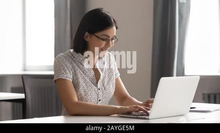 Lächelnde junge Frau in Brille, die mit dem Tippen auf dem Laptop arbeitet Stockfoto