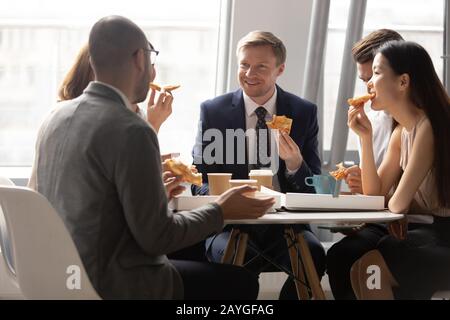 Multiethnische Kollegen sprechen in der Mittagspause über Pizza und Kaffee Stockfoto
