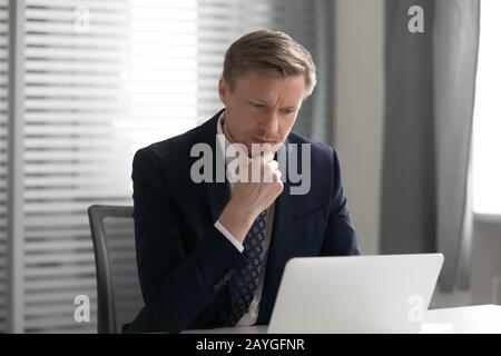 Peniente männliche Angestellte, die Laptops verwenden, wenn sie die Geschäftsidee berücksichtigen Stockfoto