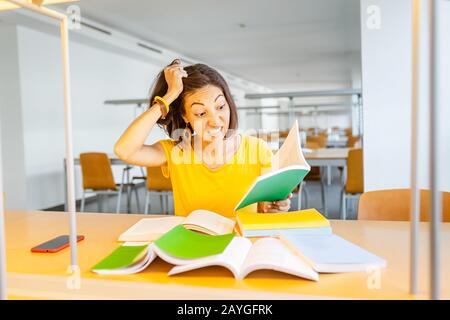 Wütende und gestresste Frau, die mit Büchern am Tisch sitzt. Krank und müde vom Bildungskonzept Stockfoto