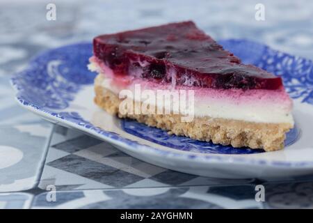 Slice Sommerfrucht-Käsekuchen mit Keksbasis auf einem blau-weiß verzierten Teller. Mit blau gemustertem, gefliesten Arbeitsplatten Stockfoto