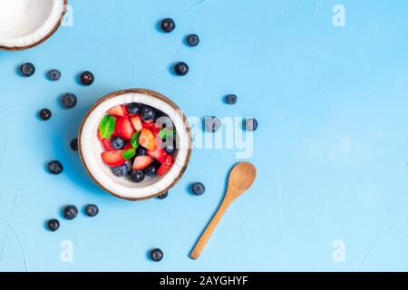 Gesundes Frühstückskonzept. Kokosschale mit frischen Beeren auf blauem Grund. Draufsicht mit Kopierbereich Stockfoto