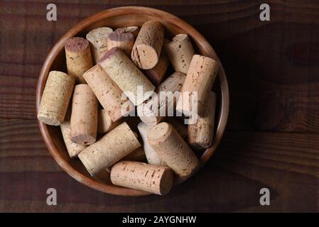 Hochwinkeliger Schuss einer Wooenschüssel voller gebrauchter Weinkorken auf einem dunklen Holztisch mit Kopierraum. Stockfoto