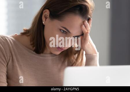 Nachdenkliche junge Frau fühlt sich bei der Arbeit am Laptop nachdenklich an Stockfoto