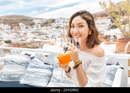 Glückliche asiatin, die aperol Spritz-Cocktail in einem griechischen Café genießen. Getränke- und Erfrischungskonzept Stockfoto