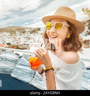 Glückliche asiatin, die aperol Spritz-Cocktail in einem griechischen Café genießen. Getränke- und Erfrischungskonzept Stockfoto