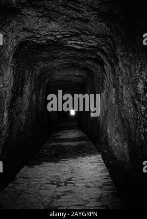 Der Wanderweg führt durch den eckigen Tunnel zum Ausgang. Der Tunnel besteht aus vulkanischen Felsen auf der Insel Madeira, und der Weg ist mit Steinen gepflastert. Schwarz Stockfoto