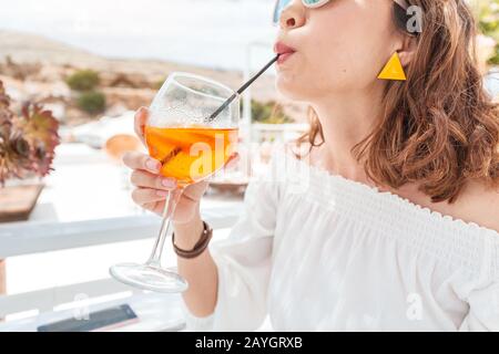 Glückliche asiatin, die aperol Spritz-Cocktail in einem griechischen Café genießen. Getränke- und Erfrischungskonzept Stockfoto