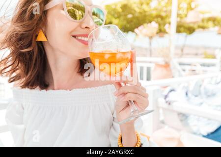 Glückliche asiatin, die aperol Spritz-Cocktail in einem griechischen Café genießen. Getränke- und Erfrischungskonzept Stockfoto