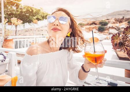 Glückliche asiatin, die aperol Spritz-Cocktail in einem griechischen Café genießen. Getränke- und Erfrischungskonzept Stockfoto