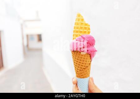 Eiskegel in der Hand auf dem Hintergrund der weißen Straßenstadt. Reisedesert und Diätkonzept Stockfoto