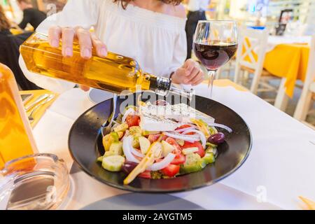 Frau gießt Olivenöl in griechischen frischen Salat im Restaurant Stockfoto
