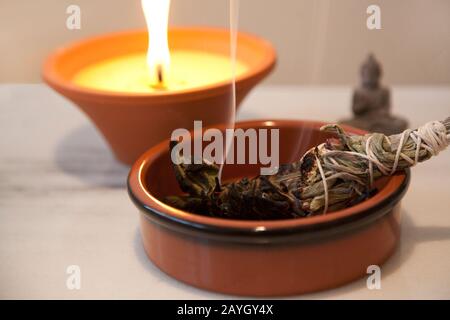 Zeremonielle weiße Salbe mit einem im Hintergrund brennenden Kerzenflammen brennender Smudge-Stick Stockfoto