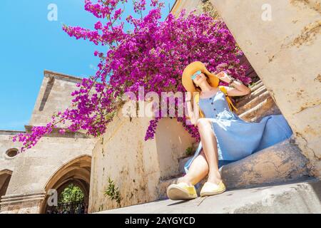 Elegante Frau im Hut, die in der Nähe von blühenden violetten Blumen posiert Stockfoto