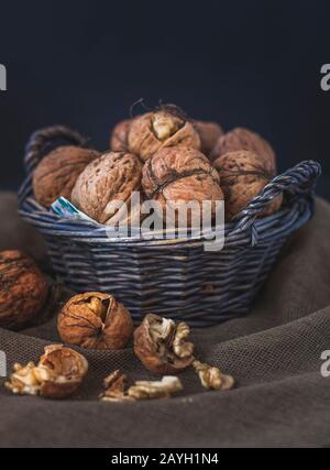 Reife Nüsse in einem Korbkorb auf dunklem Hintergrund. Einige Muttern sind gespalten. Die stimmungsvolle Atmosphäre schafft magisches Licht und eine rustikale Leinwand auf der Unterseite. Stockfoto