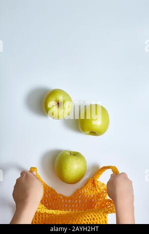 Äpfel fallen in einen offenen gelben Sack mit Netzschnur, weibliche Hände im Rahmen. Auf weißem Hintergrund mit Kopierbereich. Stockfoto