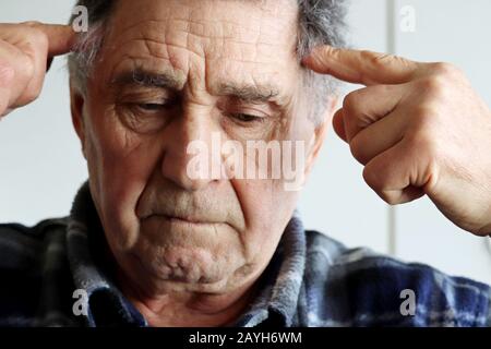 Der ältere Mann massiert die Tempel mit den Händen. Porträt des männlichen Denkens über etwas, Konzept der mentalen Aktivität im Alter, Erinnerung, Kopfschmerzen Stockfoto