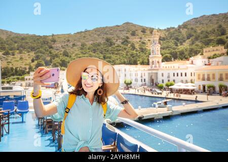 Junge asiatin Touristin macht selfie Foto mit dem Kloster Panoramitis auf dem Hintergrund vom Kreuzfahrtschiffdeck. Stockfoto