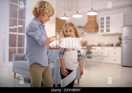 Zwei Kinder spielen zu Hause Toilettenpapier Mama und schauen unterhalten Stockfoto