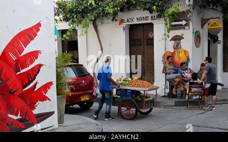 Obsthändler und Menschen, die sich außerhalb der Black Parrot Bar in Getsemani, Cartagena, Kolumbien unterhalten Stockfoto