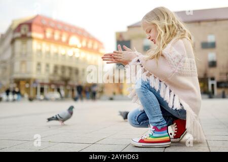 Süßes kleines Mädchen, das am Frühlingstag Vögel füttert. Kind füttert Tauben und Spatzen im Freien. Aktive Freizeit mit Kindern. Stockfoto