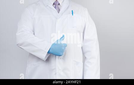 Doktor in einem weißen Mantel und Krawatte zeigt mit der Hand eine Geste wie, trägt blaue Latex-Medizinhandschuhe, weißen Hintergrund, Kopierraum Stockfoto