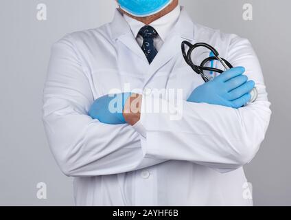 Erwachsener männlicher Arzt in einem weißen medizinischen Mantel steht und hält ein schwarzes Stethoskop auf weißem Grund Stockfoto