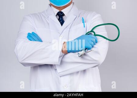 Erwachsener männlicher Arzt in einem weißen medizinischen Mantel steht und hält ein grünes Stethoskop auf weißem Grund Stockfoto