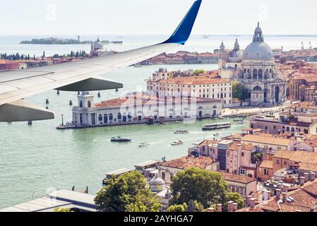 Flugzeug fliegt über Venedig, Italien. Luftpanorama von Flugzeugfenster aus auf Stadt und Meer. Der Flugzeugflügel über Venedig beim Start oder bei der Landung Stockfoto