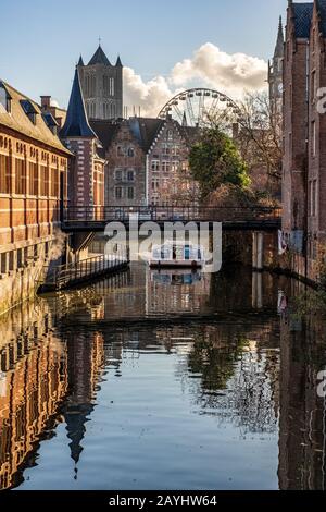 Ein Flussboot am Kanal in Gent mit einem Riesenrad und der St. Nikolauskirche im Hintergrund Stockfoto