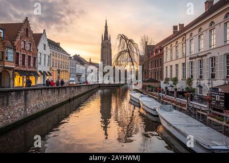 Ein Blick auf den Fluss und Reflexionen der Liebfrauenkirche Brügges (Onze Lieve Vrouw Brugge) sowie Flussboote bei Sonnenuntergang Stockfoto