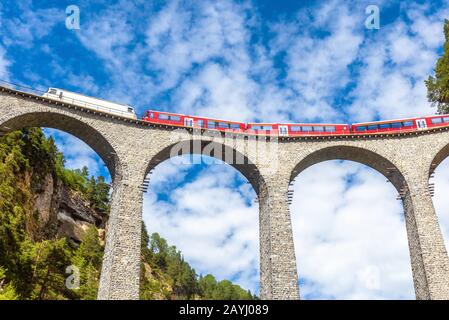 Landwasser Viadukt in der Nähe, Schweiz. Sie ist das Wahrzeichen der Schweizer Alpen. Der rote Schnellzug fährt auf hoher Brücke in den Alpenbergen. Fantastischer Blick auf den Fam Stockfoto