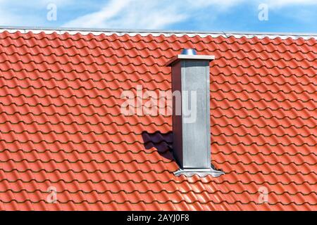Kamin auf sauberem Dach des Wohnhauses. Metallschornsteinrohr auf dem Hintergrund roter Fliesen. Modernes Belüftungssystem auf dem Dach. Kamin aus Stahl geschlossen Stockfoto