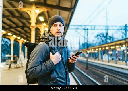 Sopot fast Urban Railway Station: Junger Mann steht und wartet auf dem Bahnsteig. Touristenfahrten mit dem Zug. Porträt Des Kaukasischen Männers In Der Eisenbahn Stockfoto