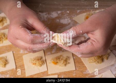 Eine Frau sculpt Knödel und Ravioli aus Kneten und Kohl. Sperrholzschneidplatte, Holzmehlsieb und Walzstift aus Holz - Werkzeuge für Stockfoto