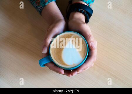 Weibliche Hände umarmen einen großen Becher mit Cappuccino. Stockfoto