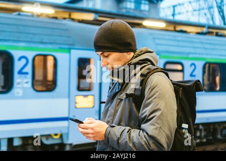 Sopot fast Urban Railway Station: Junger Mann steht und wartet auf dem Bahnsteig. Touristenfahrten mit dem Zug. Porträt Des Kaukasischen Männers In Der Eisenbahn Stockfoto