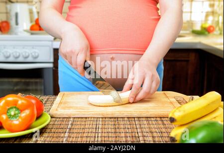 Schwangere bereitet eine Banane in der Küche zu. Gesunde Ernährung. Stockfoto