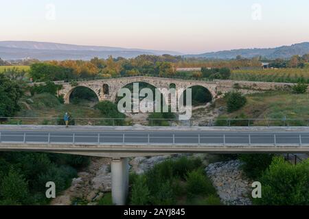 Blick auf die Pont Julien ist eine römische Steinbogenbrücke über den Fluss Calavon in der Provence in Südfrankreich aus dem Jahr 3 v. Chr. mit der modernen roa Stockfoto