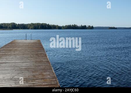 Holz-Schwimmdock-Pier mit Metallleiter am ruhigen blauen See sonniger Tag in der Natur Finnland idyllischer Naturort Stockfoto