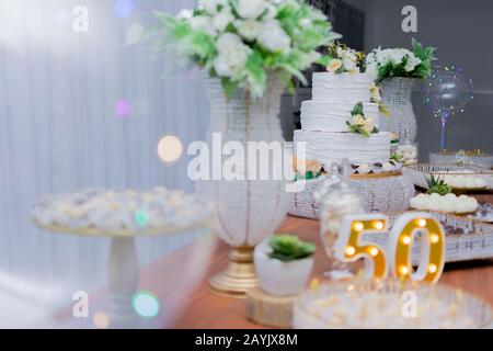 Ein schöner Kuchen zum 50-jährigen Jubiläum dekoriert. Tischgeburtstag mit einem zweilagigen weißen Kuchen, der mit gelben Rosen und grünem grünen Kleie verziert ist Stockfoto