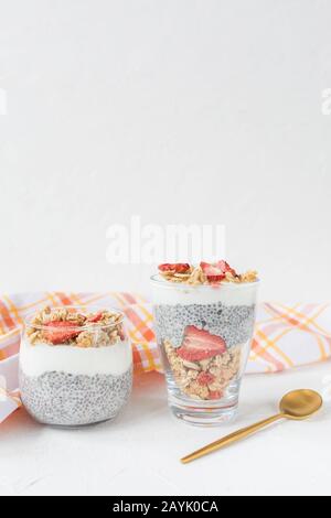 Übernachtung mit chia Seed Pudding mit Mandelmilch, Joghurt, hausgemachter Granola, getrockneten Erdbeeren und Mandeln in zwei Gläsern und Löffel. Superfood und Veganer Stockfoto