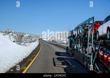 LKW-Anhänger transportiert neue Autos Fahrten auf der Landstraße mit schneebedeckter Landschaft in den Bergen Stockfoto