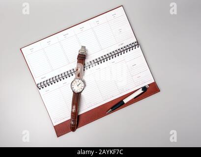 Geschlossenes Notebook in Lederbindung mit Stift und Uhr auf grauem Hintergrund. Platz für Text. Stockfoto