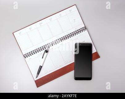 Ein offenes Notebook in Lederbindung mit Smartphone und Stift auf grauem Hintergrund. Platz für Text. Stockfoto