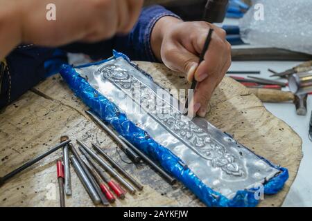 Thailändisches Muster auf Metallplattenschnitzerei durch professionelle Handwerker, um lokale traditionelle handgefertigte handgefertigte Kunstwerke zu machen Stockfoto