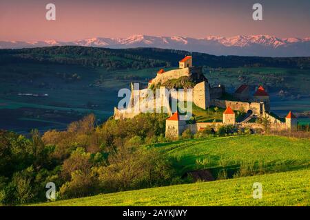 Majestätische Festung Rupea auf dem Hügel, schöne Befestigungsanlage und hohe verschneite Berge im Hintergrund, Brasov, Siebenbürgen, Rumänien, Europa Stockfoto