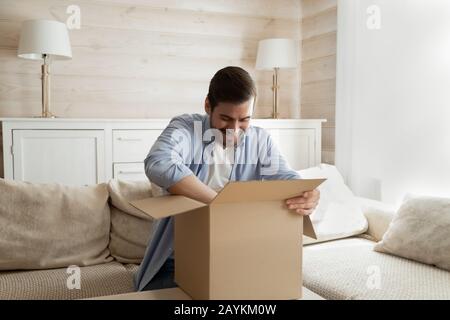 Aufgeregter männlicher Kunde entpackt Internetzustellungspaket Stockfoto