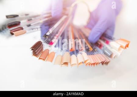 Frauenklient wählt Farbmaniküre Fake Nail polish Lack aus Palette, weißer Hintergrund Stockfoto